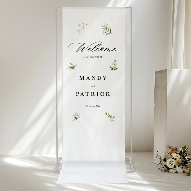 Beautiful calligraphy wedding welcome sign printed on white linen for hanging with white flowers and greenery.